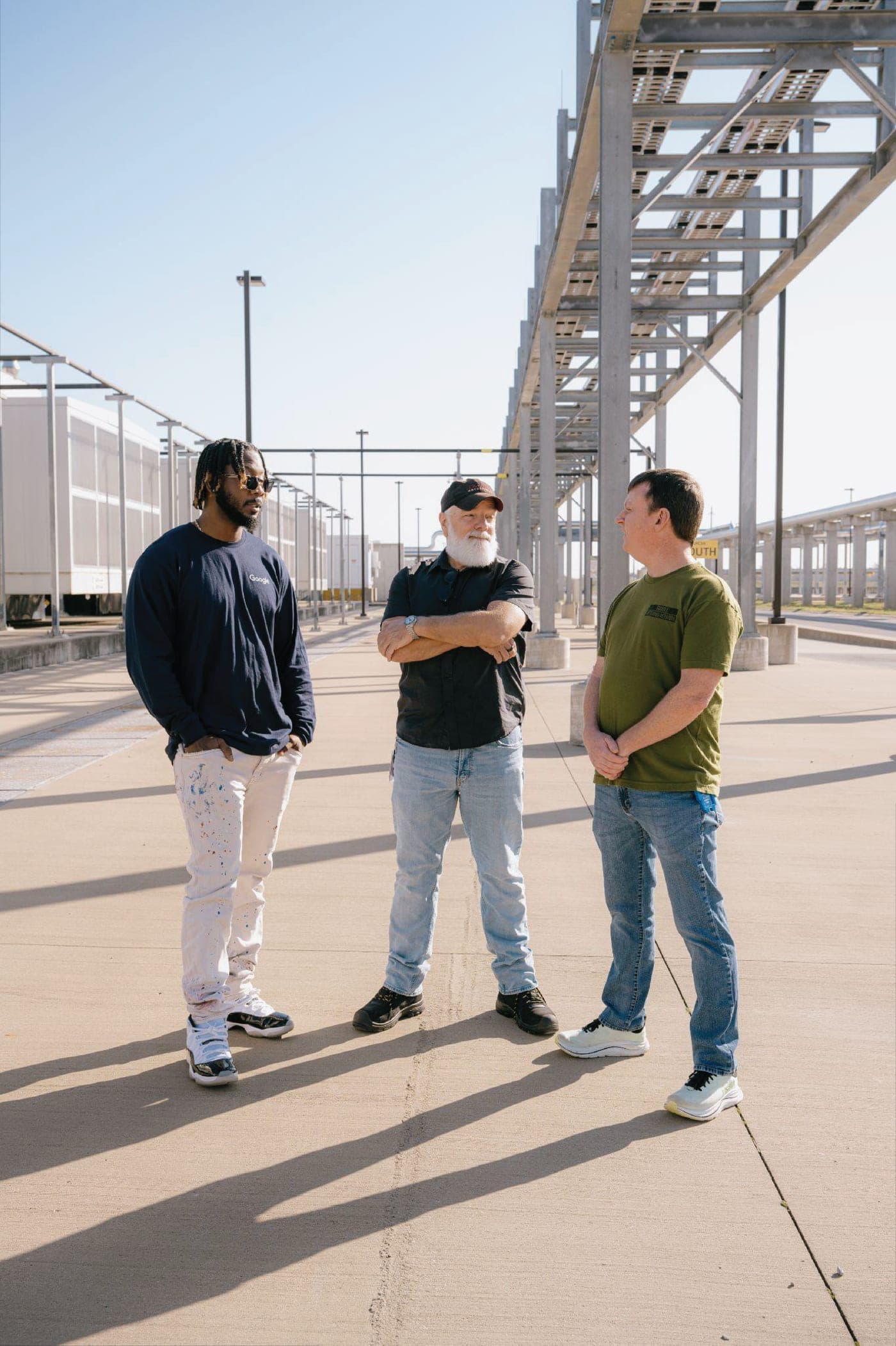 Three construction workers talking on site beside a steel-framed building